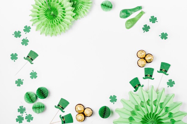 Decorations and props for St.Patrick 's Day party. Green and gold paper decorations, hat, balloons, confetti, candy and lucky symbols on white background. Festive concept. Flat lay, top view.