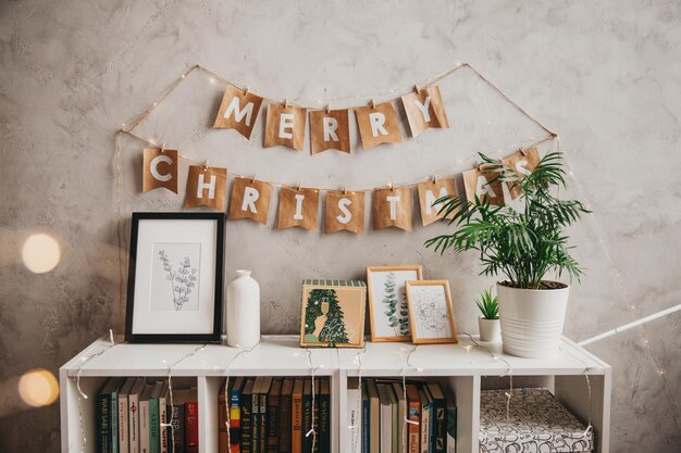 Decorazioni con la scritta buon natale su uno scaffale con libri e una parete di fondo bianca. decorazioni natalizie.