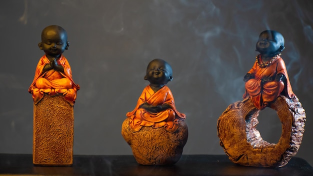 Photo decorative baby monk sitting on rock and chanting statue black background orange cloth wearing