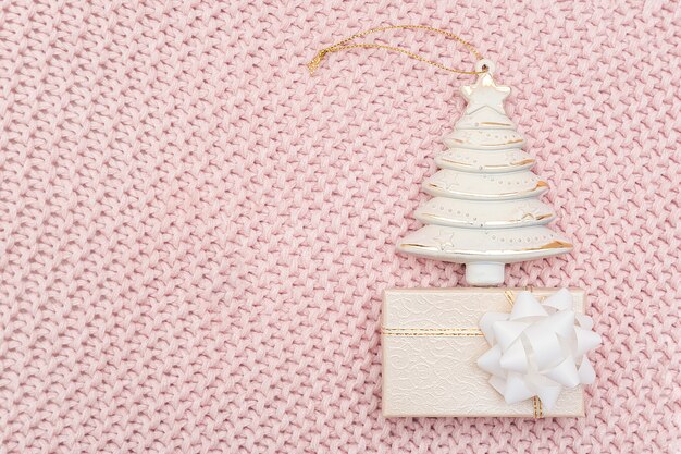 Albero di natale e contenitore di regalo beige decorativi su fondo tricottato rosa.