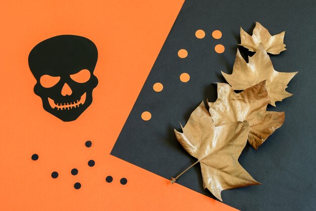 Decorative black scull, peas and golden maple leaves on the paper Halloween background