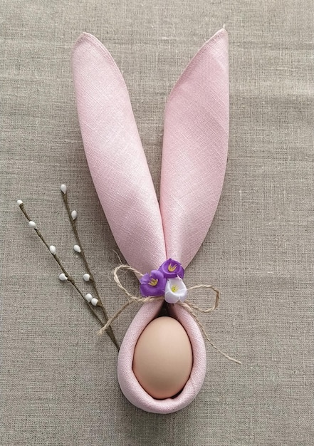 Decorative Bunny Ears from napkin with egg on natural cotton tablecloth to Celebrate Easter