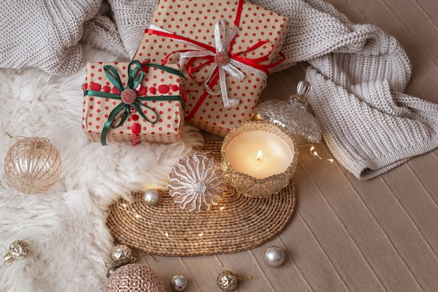 Декоративная горящая свеча на фоне рождественских подарков с уютными вещами и деталями декора крупным планом.