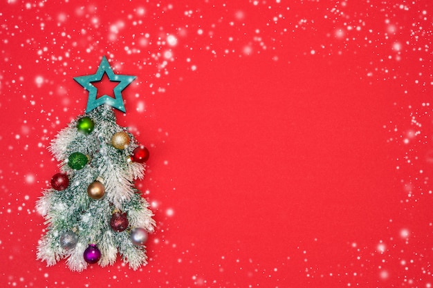 Decorative Christmas tree with Christmas ornaments on red background with snow texture. 