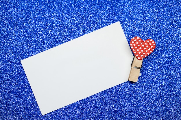 Decorative clothespin with heart and white empty sheet on blue surface