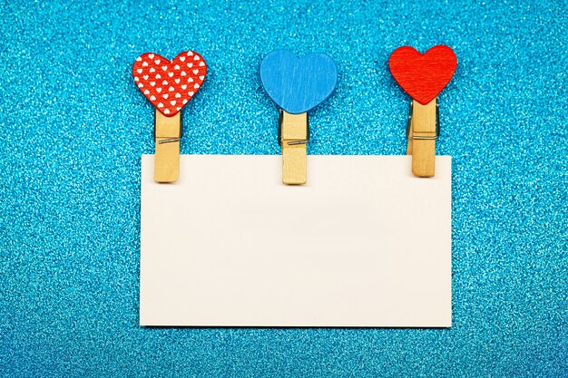 Decorative clothespins with heart and white empty sheet on blue surface