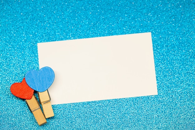 Decorative clothespins with heart and white empty sheet on blue surface