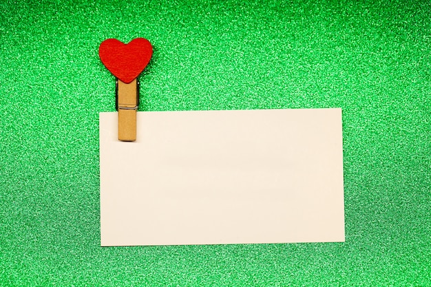 Decorative clothespins with heart and white empty sheet on green surface