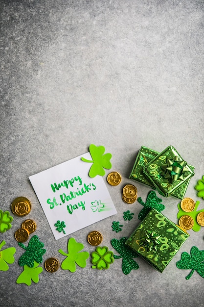 Decorative clover leaves, green gifts box, coins on stone background, flat lay. St. Patrick's Day celebration. Card Happy St. Patrick's Day