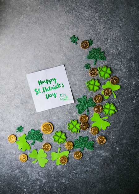 Decorative clover leaves, green gifts box, coins on stone background, flat lay. St. Patrick's Day celebration. Card Happy St. Patrick's Day