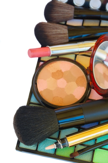 Cosmetici colorati decorativi per il trucco - rossetto, pennelli e polvere sul bordo della tavolozza ombretto isolato su priorità bassa bianca