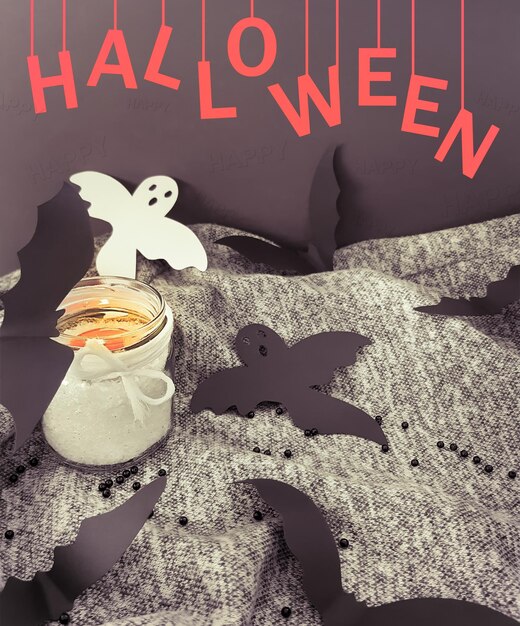 Photo decorative composition for halloween. top view, burning candle in a bottle, bats, ghosts from paper, inscription halloween, copy space for your text