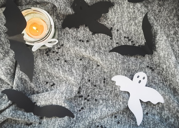 Photo decorative composition for halloween. top view, burning candle in a bottle, bats, ghosts from paper, scarf, copy space for your text