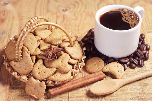 Decorative cookies in wicker basket and cup of hot coffee on old wooden table