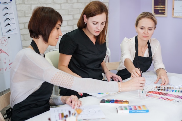 Lezione teorica di cosmetologia decorativa. signore che studiano i colori, usando tavolozza, pittura e pennelli.