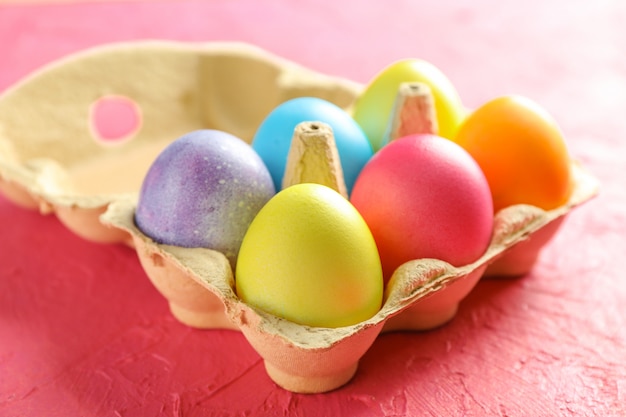 Decorative eggs in cardboard box on color background. Closeup