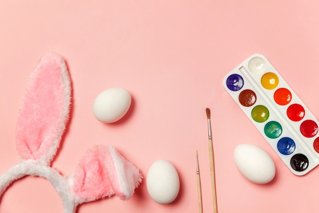 Decorative eggs colorful paints and bunny ears furry costume isolated on pink table