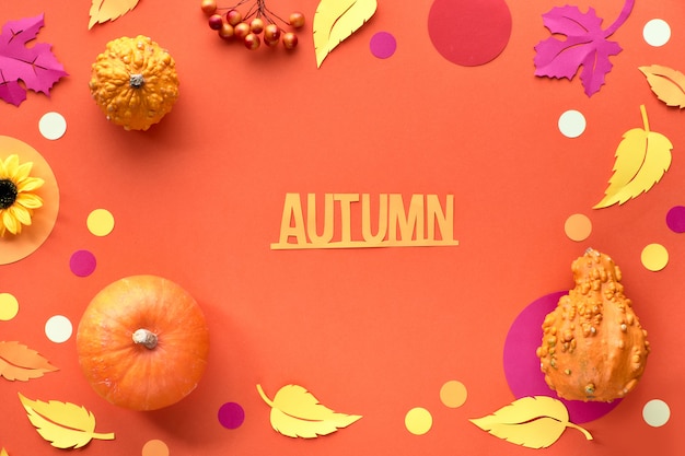 Decorative Fall flat lay, top view on orange paper background with text "Autumn", pumpkins and paper leaves