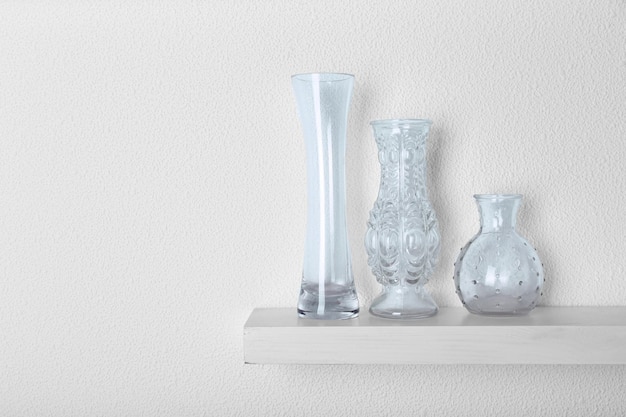 Photo decorative glass vases on wooden shelf on white wallpaper background