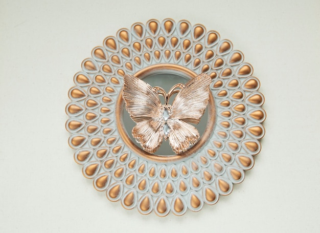 Декоративная золотая бабочка лежит на круглом зеркале