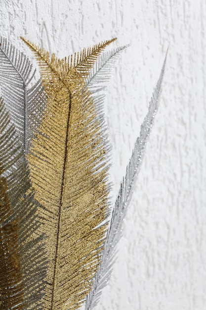 Decorative golden and silver glitter leaves on white textured wall