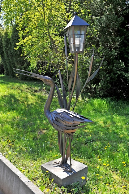 Декоративная кованая цапля из железа с фонарем в парке