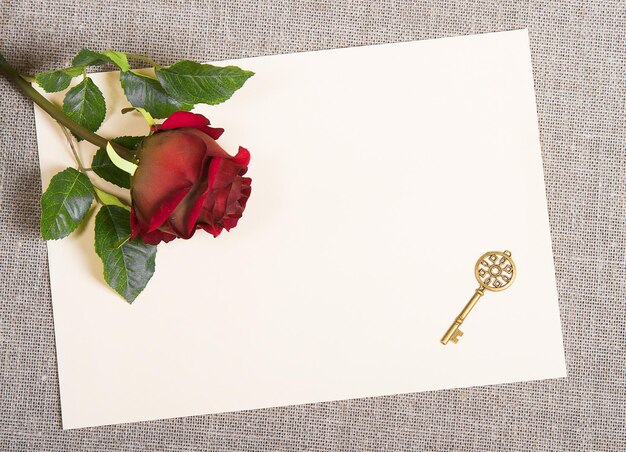 Decorative key and red rose on a blank paper