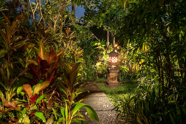 Decorative lamp on the stone pillar next to the path in the tropical garden at night . Ubud, island Bali, Indonesia . Nature concept