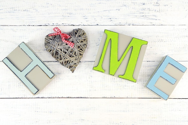 Декоративные буквы, образующие слово ДОМ с декоративным сердцем на деревянном фоне