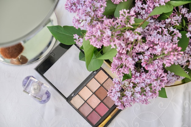 Decorative makeup cosmetics, bottle of perfume, eye shadow, fresh lilac flowers