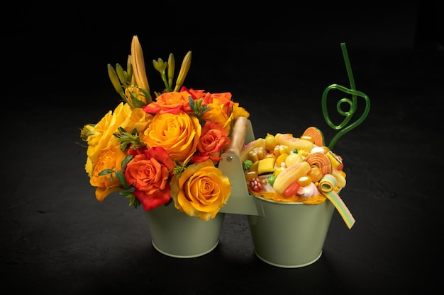 写真 オレンジ色の花とさまざまな形の甘いキャンディーで満たされた装飾的な金属製のバケツ