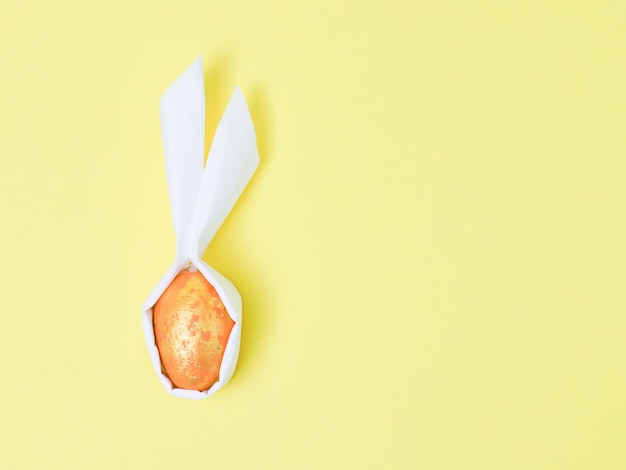 A decorative orange marbled egg with diy paper white ears on a yellow background