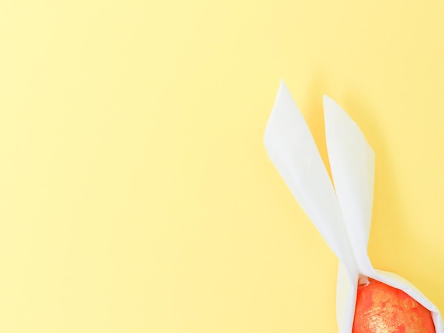 A decorative orange marbled egg with diy paper white ears on a yellow background