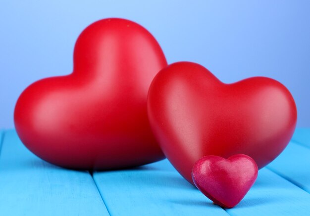 Decorative red hearts on blue wooden table on blue background