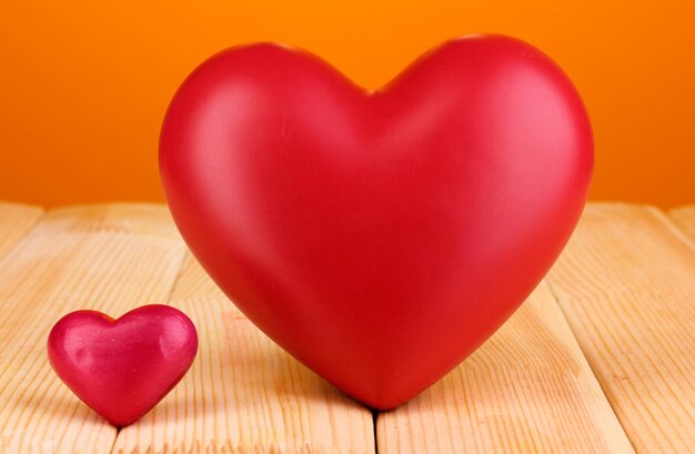 Decorative red hearts on wooden table on orange background