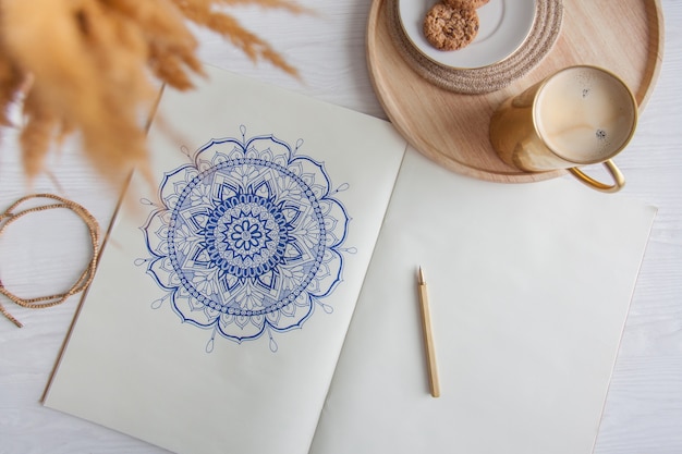 Mandala floreale rotondo decorativo disegnato su un foglio bianco. casa relax, hobby e riposo. caffè e biscotti su uno sfondo bianco.