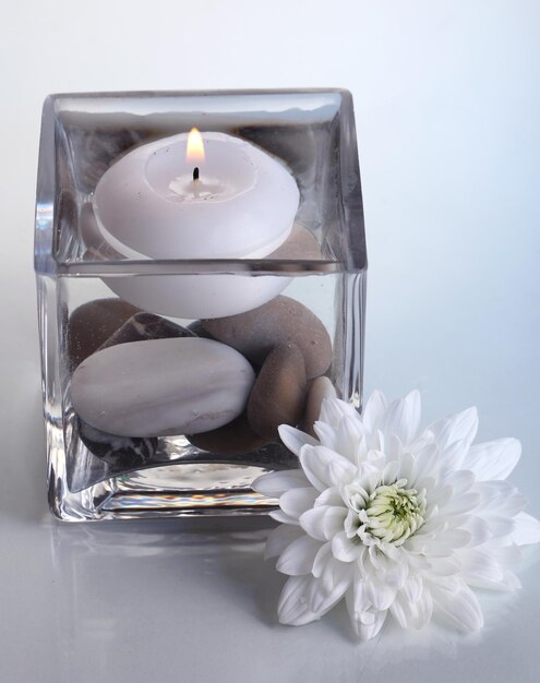 Decorative vase with candle water and stones on light blue background