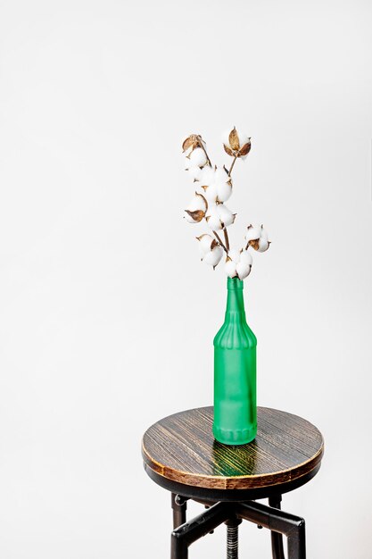 Decorative vase with cotton branch on wooden and metal stool