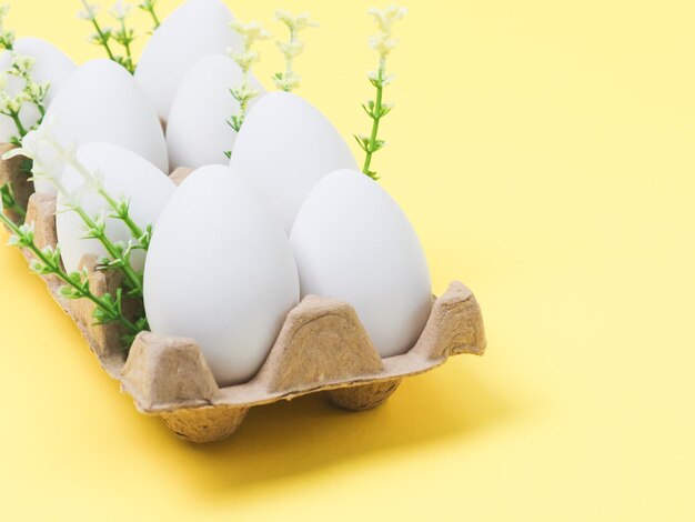 Decorative white eggs in a cardboard box with spring flowers on a yellow