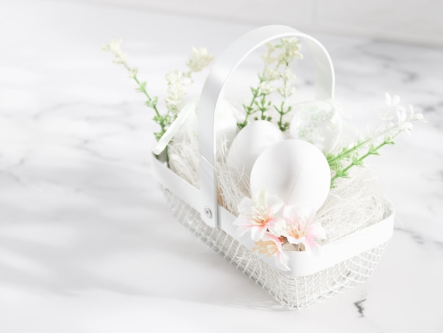 Decorative white eggs in a metal basket with eggs spring flowers and straw on a marble table