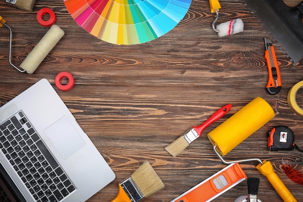 Decorator's tools and laptop on wooden background