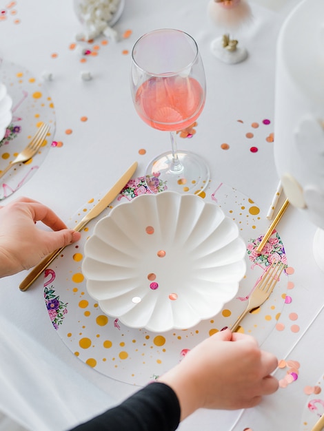 Decorator serving party table in white colors with beautiful white dishes, glasses for wine, golden cutlery. Happy birthday or baby shower for girl. Close up