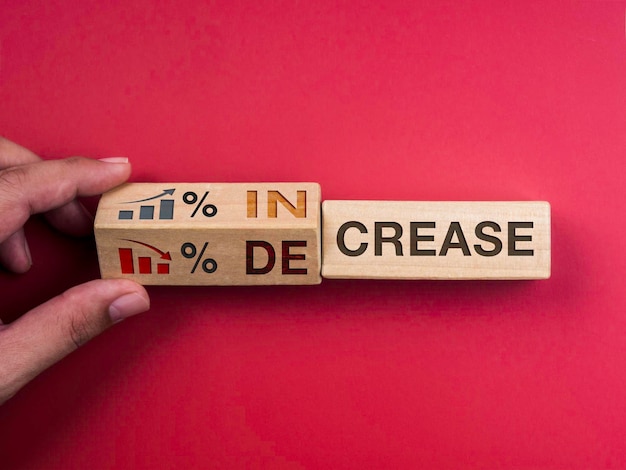 Decrease and increase percentage business concept. Words "INCREASE" on wooden block changing to "DECREASE," turning by hand with percentage symbol, growth and down chart graph icon on red background.