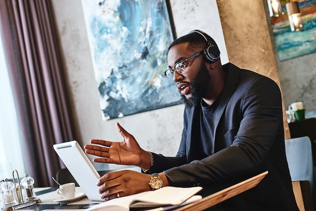 Dedicate yourself young businessman with tablet pc and headphones sitting in cafe and networking