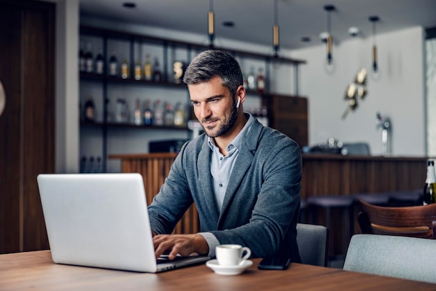 A dedicated busy man dressed in smart casual is sitting in working friendly cafe and typing a report