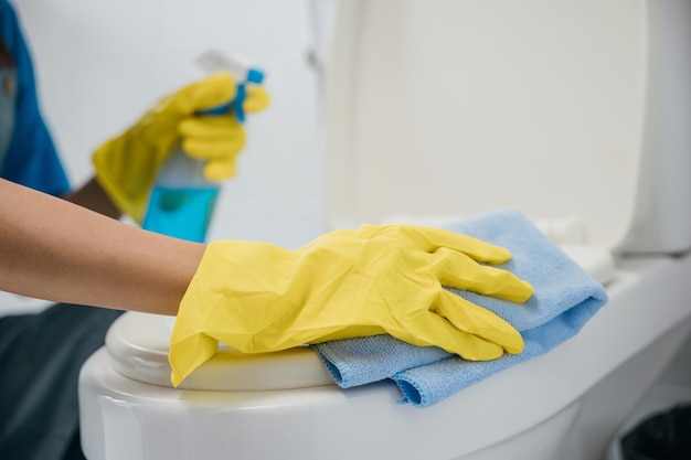Dedicated maid in rubber gloves scrubs toilet seat with cloth ensuring hygiene in the bathroom Her focus on cleanliness highlights the essence of housekeeping Housekeeper healthcare concept