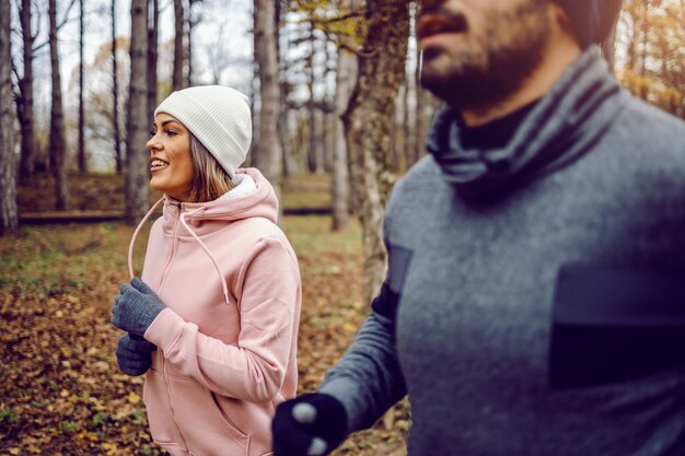 Dedicated young sporty couple in sportswear running in nature side by side on cold weather.