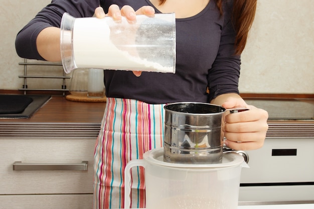 Deeg koken. Meisje voegt bloem toe aan een kom om te kloppen met een mixer in de keuken.