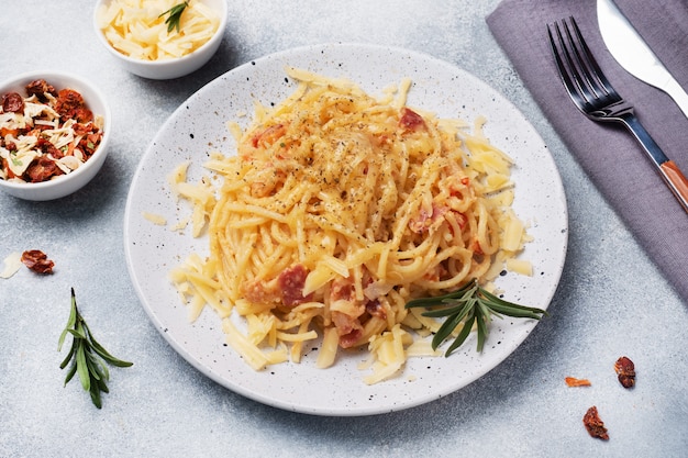 Deegwarenspaghetti met de kaas van het baconei op een plaat met kruiden. Traditioneel Italiaans gerecht Carbonara. Grijze betonnen tafel