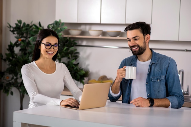 Deel je emoties Vrolijke man die thee drinkt terwijl zijn vriendin een laptop gebruikt